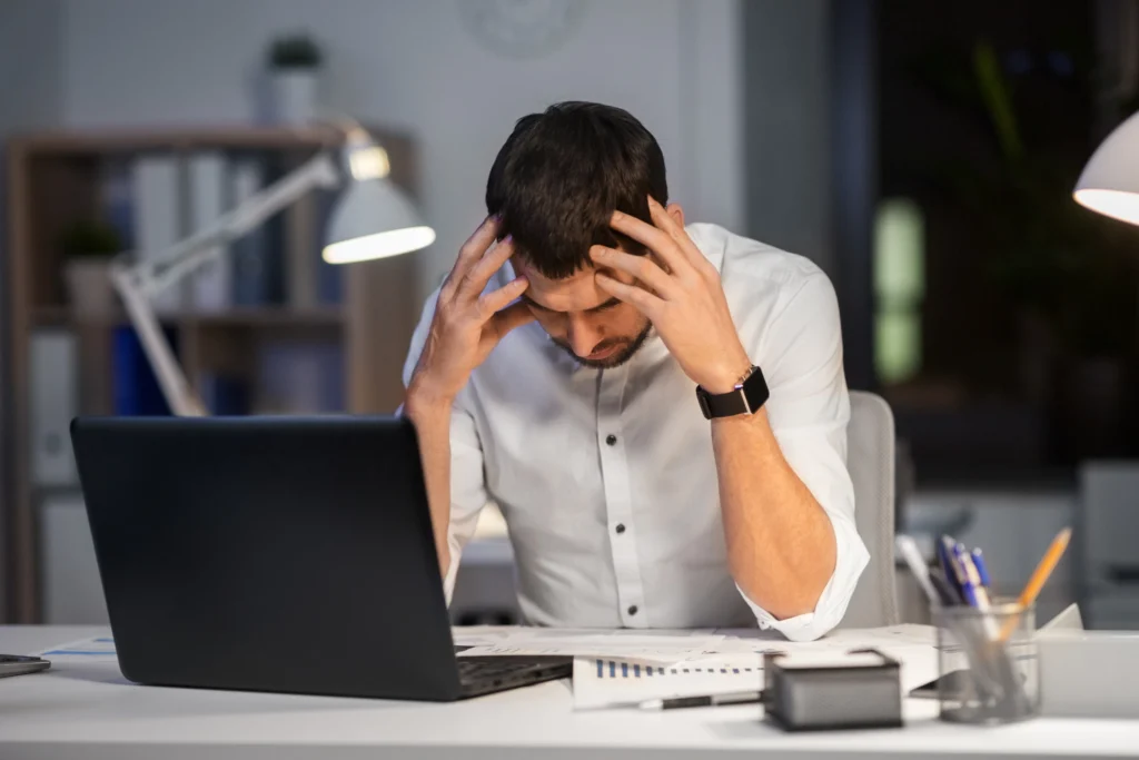 Hombre frustrado frente a su computadora mientras revisa gráficos y documentos, representando los desafíos que enfrenta un empresario cuando su página web no genera ventas.