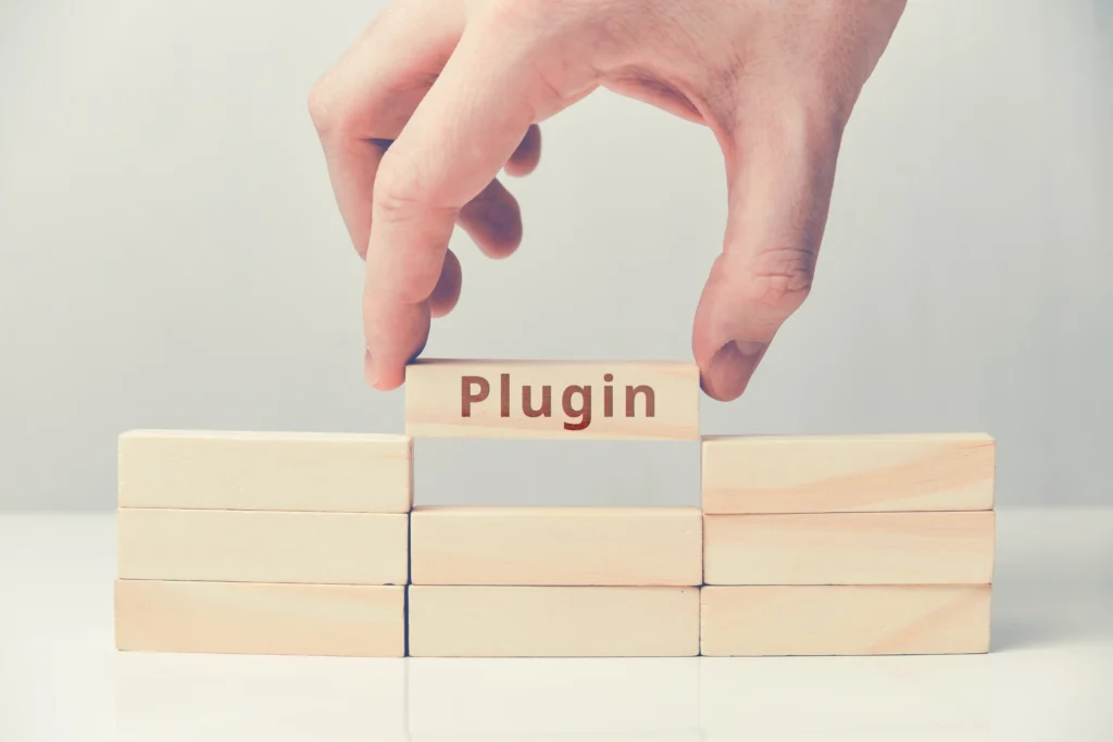 Una mano colocando un bloque de madera con la palabra 'Plugin' sobre otros bloques, representando cómo un plugin añade una funcionalidad específica a un sistema o plataforma.