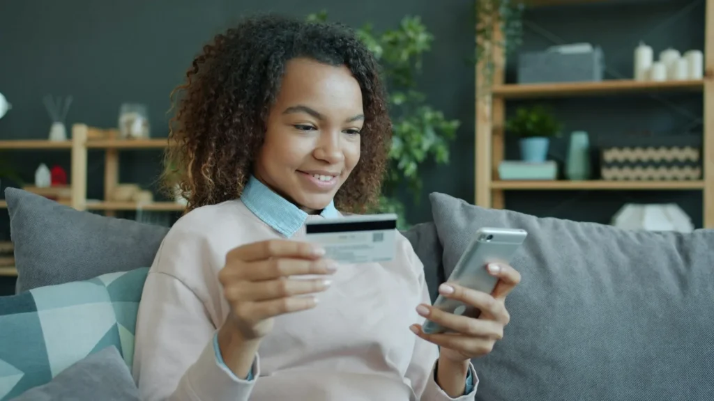Mujer joven con tarjeta de crédito y celular, lista para pagar en una tienda online