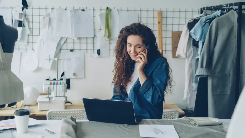 Emprendedora sonriendo al hablar por teléfono frente a su laptop en su taller