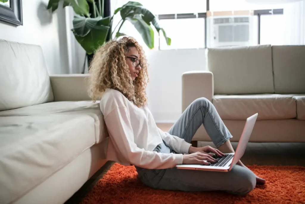 Mujer sentada en el suelo de su sala revisando el correo de su negocio en una laptop